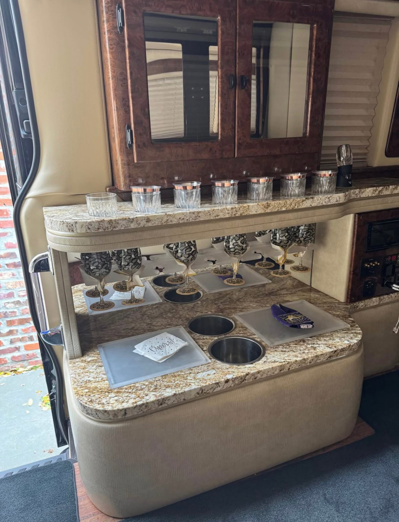 Interior view of a luxury RV kitchen featuring granite countertops, wooden storage cabinets, and a compact sink area, ideal for travel and comfort.