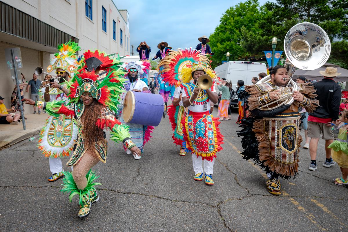 Colorful parade featuring dancers in traditional costumes and musicians playing instruments during a cultural festival in Louisiana.