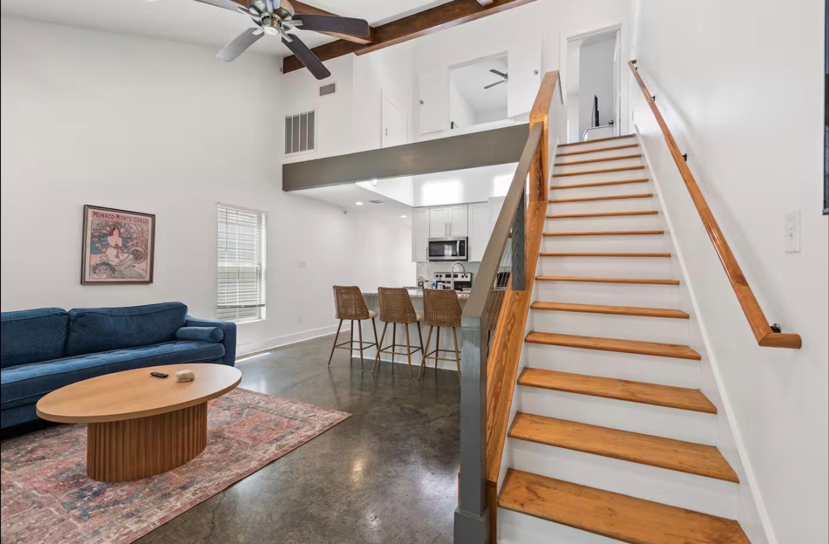 Spacious modern living room with high ceilings, white walls, wooden staircase, and a cozy blue sofa, perfect for family gatherings and relaxation.