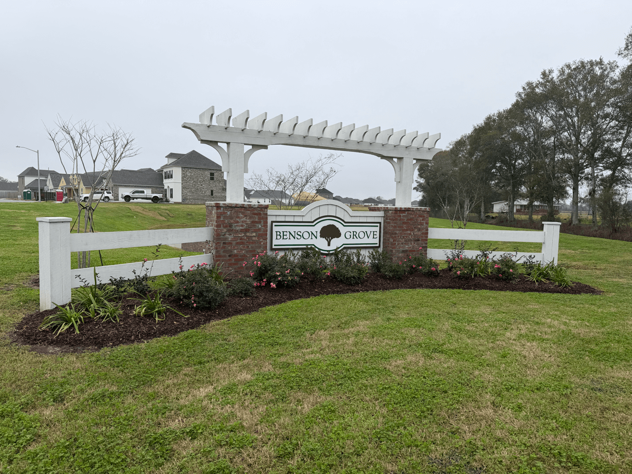Entrance sign for Benson Grove Subdivision featuring a white pergola, brick base, and landscaped surroundings, welcoming residents and visitors to the community.